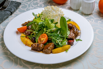 Salad with chicken liver, tomatoes and greens on white plate