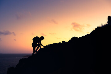Silhouette of man climbing up a mountain cliff. Goal setting, courage, and will power concept. 