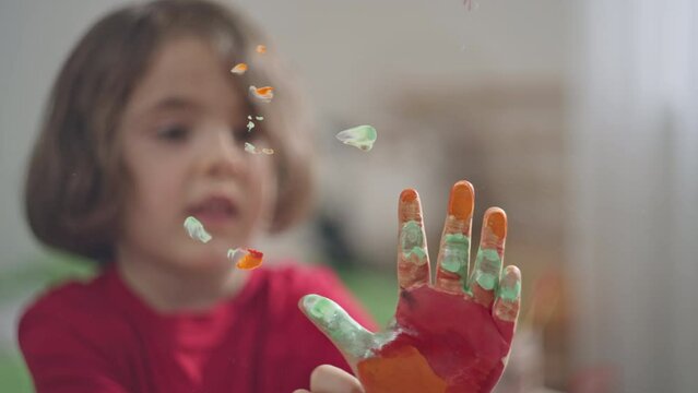Caucasian girl girl puts her handprints on the glass with paint. The girl draws handprints on the glass, happy childhood.