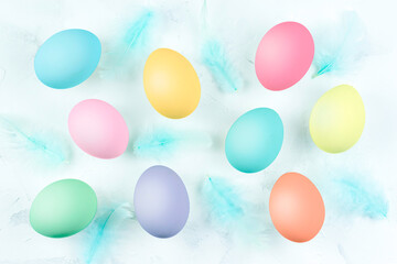 Multicolored eggs on a white textured background and blue feathers.
