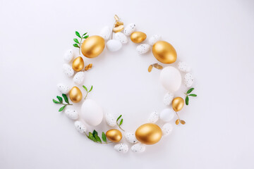 decorative golden Easter eggs abd green leafs in ring frame on a white background. Copyspace