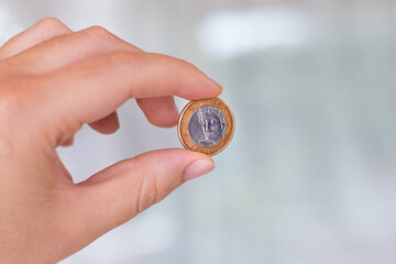 One real coin in the palm of a person's hand. Hand holding a 1 dollar coin. Real is the currency system of the Brazilian Government