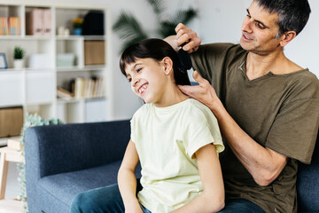 Caring father brushing his daughter hair at home. Parenthood concept.