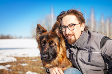 Portrait of a man with his German Shepherd dog in winter, against a blue sky.
