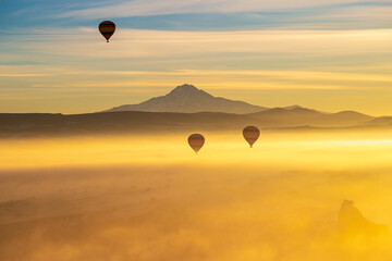 Hot air balloons flying over Cappadocia Goreme National Park Turkey with a view Erciyes mountain; foggy air