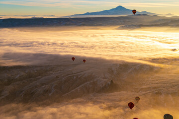 Fototapeta na wymiar Hot air balloons flying over Cappadocia Goreme National Park Turkey with a view Erciyes mountain; foggy air