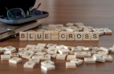 blue cross word or concept represented by wooden letter tiles on a wooden table with glasses and a book