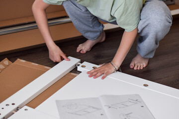 Young girl assembling new furniture using instruction manual