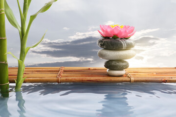 Stack of zen stones with lotus flower, pond and bamboo against cloudy sky