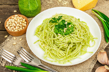 Spaghetti pasta with pesto sauce and fresh ramson leaves. Cutlery, parmesan, pine nuts. Rustic style