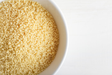Bowl of raw couscous on white background, closeup