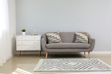 Grey sofa, chest of drawers with jug and glasses near light wall