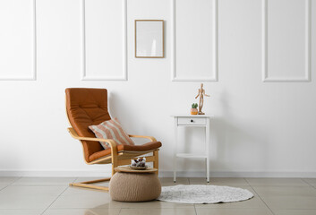 Interior of light living room with armchair, table and beige pouf