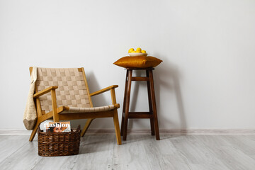 Comfortable armchair, stool and wicker basket near light wall in room interior