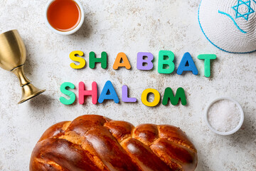 Text SHABBAT SHALOM with traditional challah bread, cup for wine and Jewish cap on grunge background