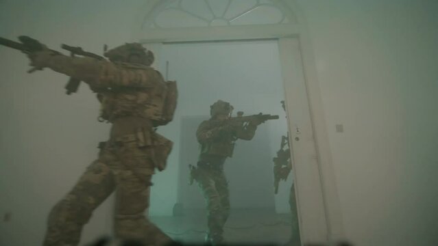 Group of men in camouflage uniform playing airsoft indoor. Front view of men entering dark room, moving forward together, covering and defending each other in building. Attack, airsoft game concept
