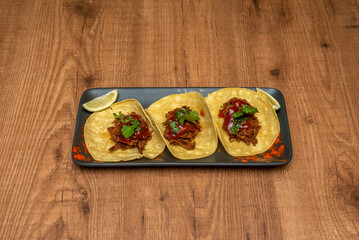 Three Mexican stewed shredded beef tacos with sauce on a black tray