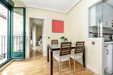 living room with open green aluminum balcony, glass and wood dining table with matching chairs and kitchen with glass cabinet