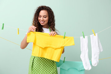 Young African-American woman hanging clean t-shirt with clothespin on color background