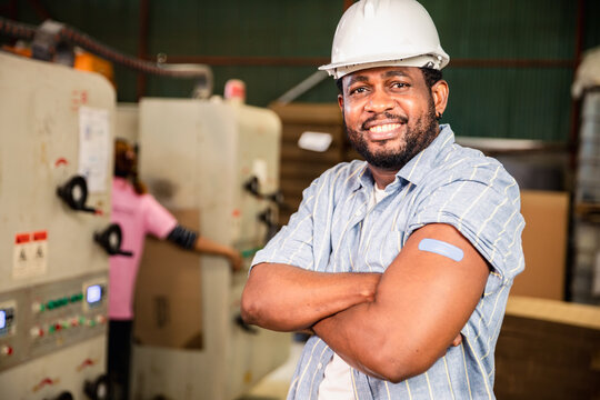 African workers  pointing at his arm with a bandage after receiving the covid-19 vaccine.Vaccination for Essential Workers in healthcare at industrial factory.