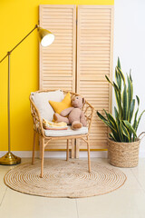 Armchair with baby clothes, toys, lamp and houseplant near color wall