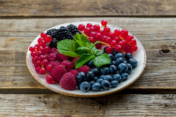 plate with fresh berries and mint on old wooden table