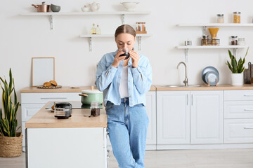 Young woman drinking tasty coffee in kitchen