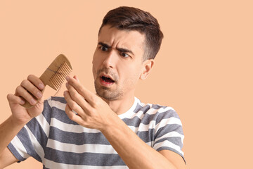 Shocked young man holding comb with fallen down hair on beige background