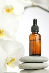 Fototapeta na wymiar Beauty and aromatherapy.Massage oil and massage stones. bottle with oil on gray stones and white orchid flower on white background.Spa and relaxation.White orchid flower, massage stones and oil 