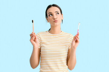 Thoughtful young woman with toothbrushes on blue background