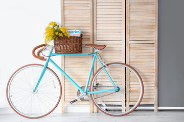 Fototapeta na wymiar Basket with mimosa flowers and magazines on bicycle near folding screen