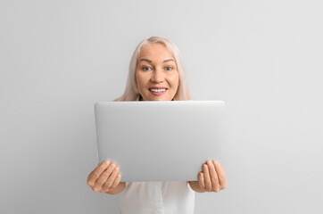 Mature secretary with laptop on light background