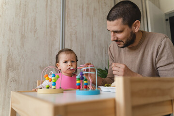 A father is feeding his daughter inside the house during the day