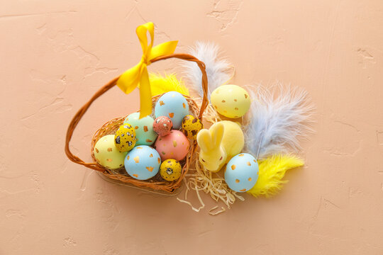 Basket with painted Easter eggs, feathers and bunny on beige background