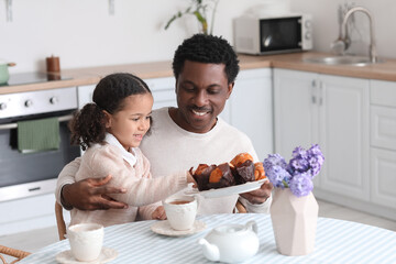 Obraz na płótnie Canvas Happy African-American man and his little daughter having breakfast in kitchen