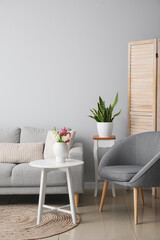 Interior of modern living room with grey sofa, armchair and flowers in vase