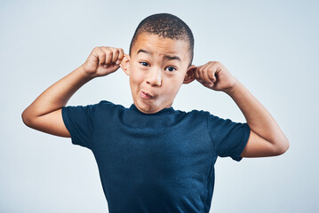 Goofy Ill show you goofy. Studio shot of a cute little boy playfully pulling his ears against a grey background.