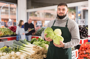 Male shop assistant in an apron carries fresh cabbage. High quality photo