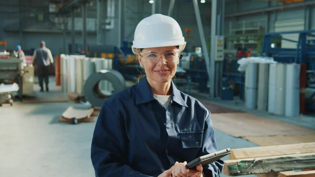 Professional woman engineers worker wearing hard hat and googles using digital tablet computer look at camera smiling in hangar. In factory