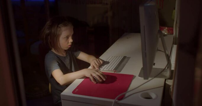 Using a teenager computer in a dark room. He presses the buttons on the keyboard. Focus of attention in the monitor. CZ, Kladno, Armenska, 27.3.22.