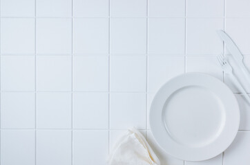 Fototapeta na wymiar Simple monochromatic white table setting with white plate, cutlery and linen napkin. White background.