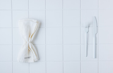 Simple monochromatic white table setting with white plate, cutlery and linen napkin. White background.