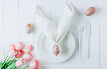 Modern dyed pink easter egg on napkin with bunny ears, flowers on plate and cutlery.