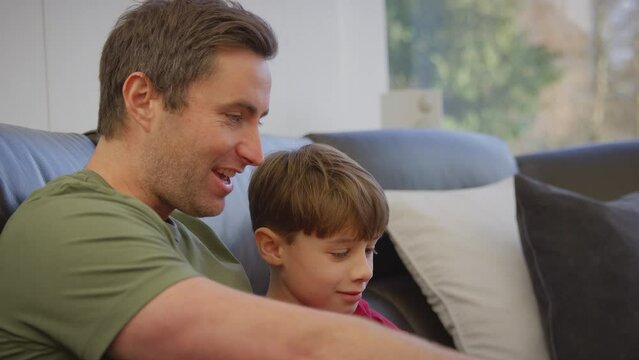 Father and son sitting on sofa at home in pyjamas together looking at laptop - shot in slow motion