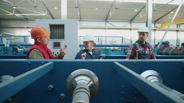 Engineers in safety uniform and hard hat walking talking. Use tablet computer and checks production processes in factory. Look around