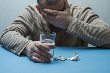 The man hides his face, medical preparations are on the table in front of him.