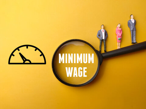 Miniature People, Magnifying Glass And Icon With Text MINIMUM WAGE On Yellow Background.