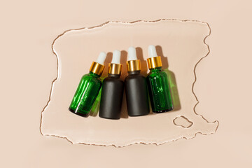 Kit of brown, green dropper glass pipette bottles on beige wet water background. Serum, oil, acid,...