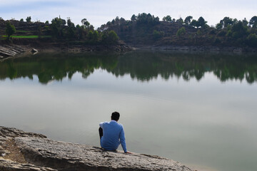 Man sitting on rock lake shore looking at peaceful view