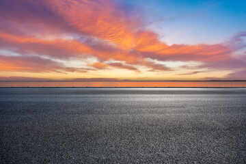 Empty asphalt road and lake with beautiful sky clouds at sunset